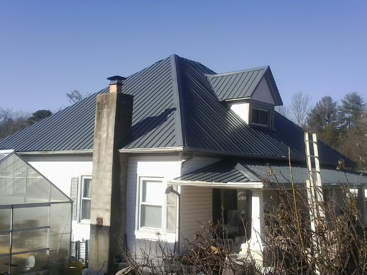Dark blue standing seam metal roof on a white farmhouse with dormer — Slate & Tile Roof Repair by Roofing Brothers in New Melle