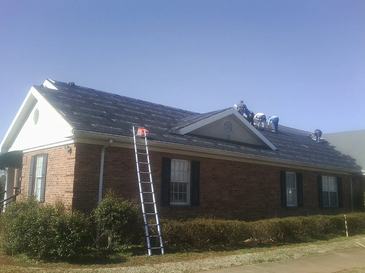 Crew tearing shingles off a brick ranch roof with a ladder set — Emergency Roof Repair work by our crew in New Melle