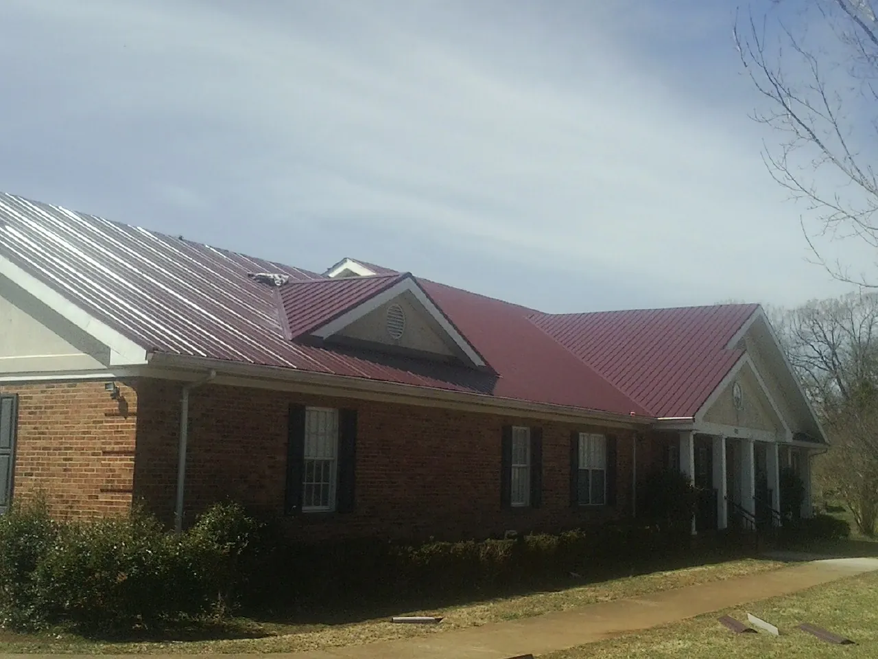 Red metal roof with gabled entries on a long brick building, from a Hail Damage Roof Repair job in New Melle