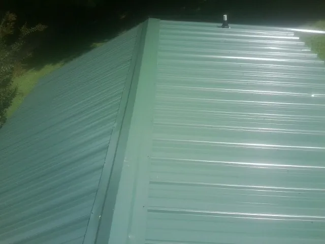 New green metal panels meeting at the ridge of a roof — Flat Roof Repair work by our crew in New Melle