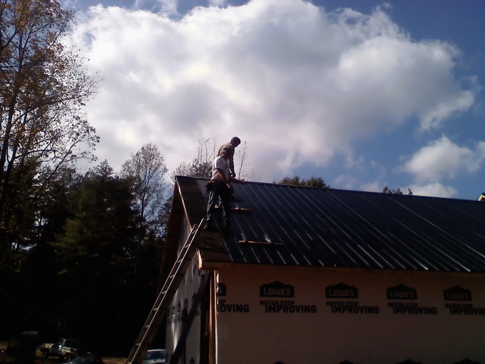 Roofer fastening dark metal panels high against a cloudy sky, from a Roof Inspection job in New Melle