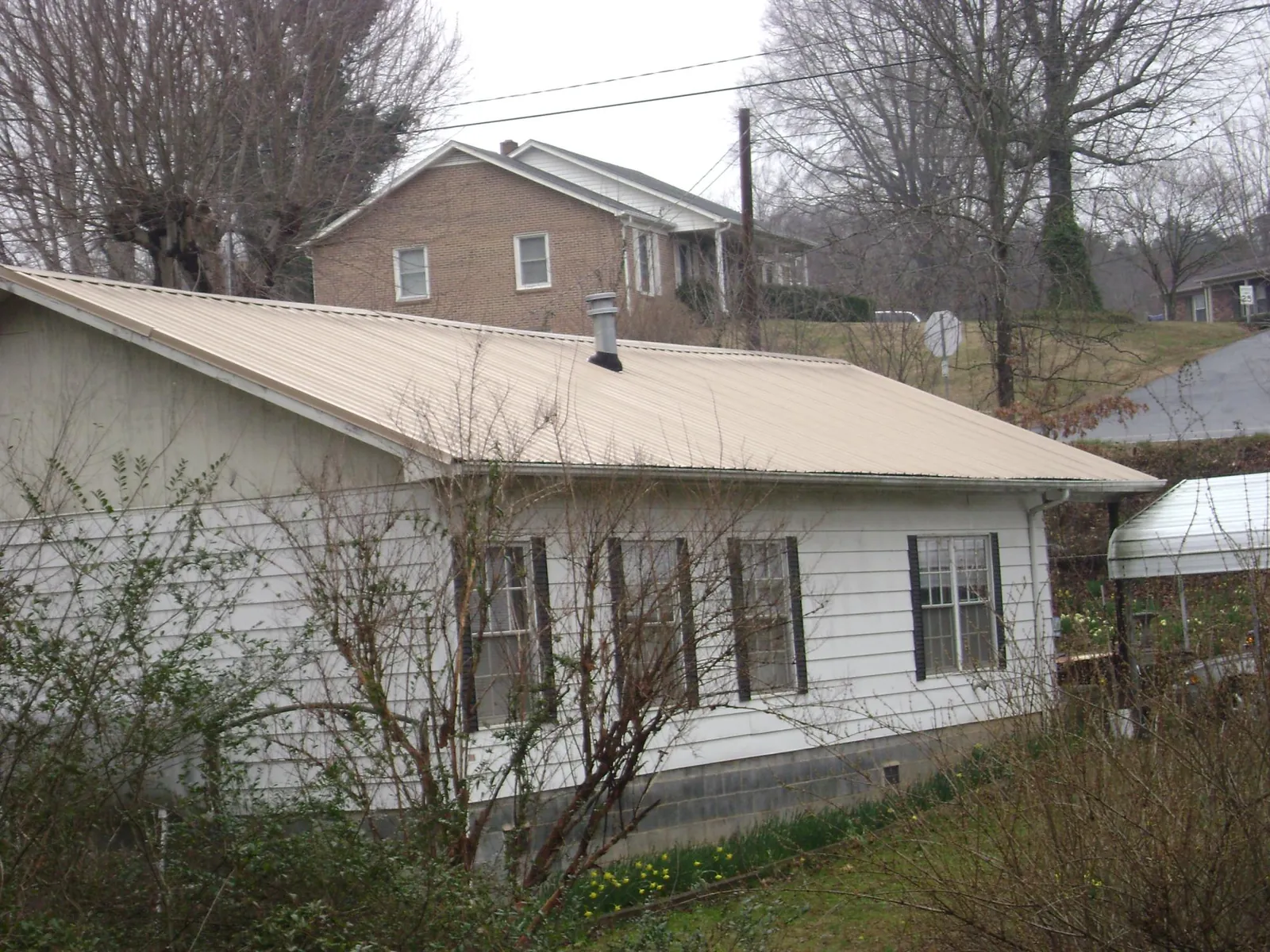 Tan metal roof on a white sided house set into a hillside — Commercial Roofing by Roofing Brothers in New Melle