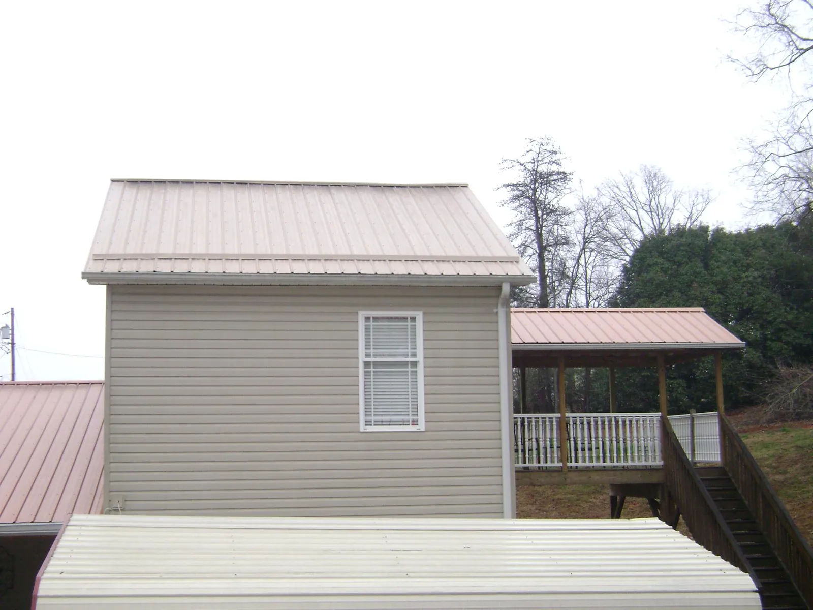 Tan metal roofs on a two story addition and attached porch, from a Roof Replacement job in New Melle